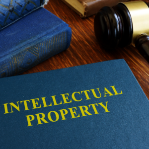 Intellectual Property written in gold writing on a blue text book with a gavel and books in the background